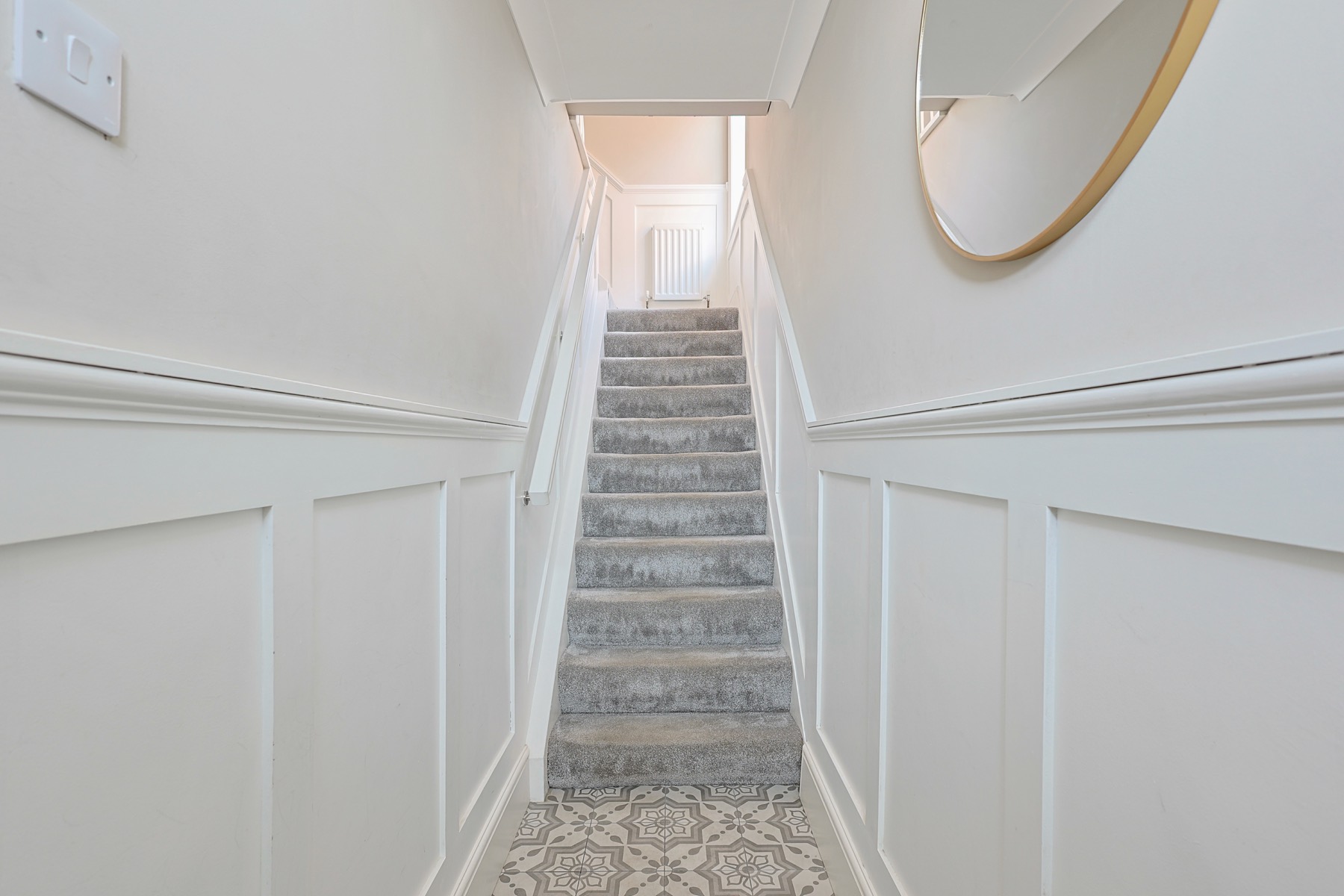 White panelled staircase with a patterned runner and a round mirror
