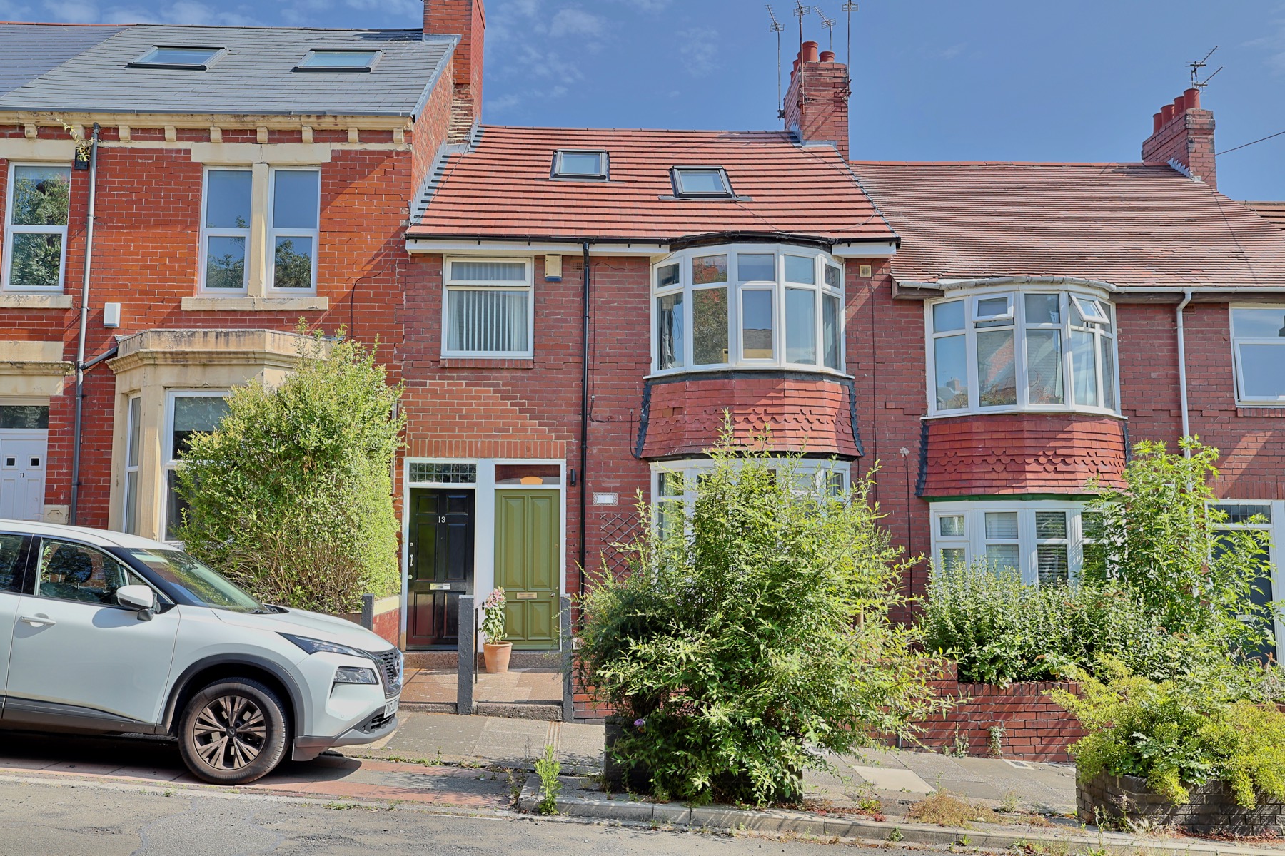 Red brick Tyneside terrace with bay windows and a green front door, photographed from the street